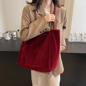 Burgundy velvet tote bag with front pocket worn by a model in a cafe setting