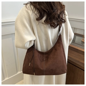 Detail of a large dark brown suede hobo bag with white stitching on a stylish wool coat