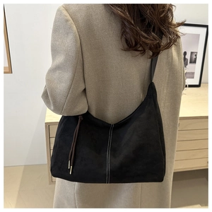 Detail of black suede tote bag with white contrast stitching and brown knot charm decoration