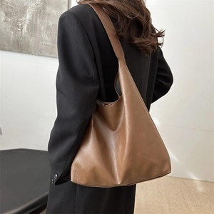 Minimalist caramel brown leather tote bag with wide strap worn on female shoulder