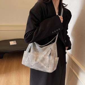 Large dark grey hobo tote bag with zipper details worn by a model in a minimal setting