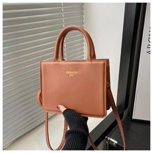 Détail d'un sac à main carré marron caramel avec poignée ronde et texte doré élégant