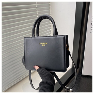 Détail d'un petit sac carré en cuir noir mat avec inscription dorée et poignée ronde