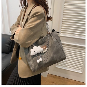 Detail of grey canvas tote bag with brown leather straps, plush cloud charm and pearl chain
