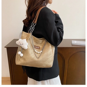 Detail of a large khaki tote bag with gold chain strap and a white plush cloud charm