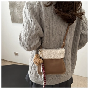 Détail d'un sac seau en cuir marron avec rabat en peau lainée blanche et breloque