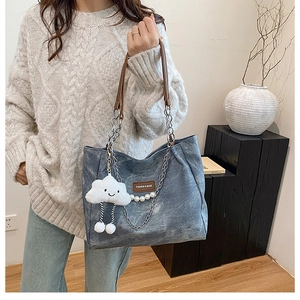 Detail of blue denim tote bag featuring brown leather strap and plush cloud charm