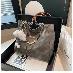 Close-up of gray canvas tote bag featuring chain handles and plush cloud charm