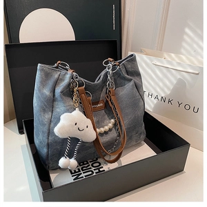 Detailed view of grey tote bag with pearl chain and cloud plush charm in a gift box