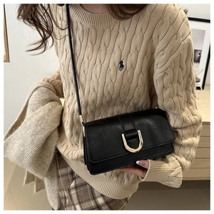 Detail of black leather crossbody bag featuring gold horseshoe buckle and textured finish