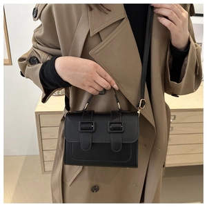 Classic black leather crossbody bag with double buckle flap shown on a trench coat