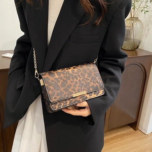 Minimalist leopard print crossbody bag with gold chain strap shown on model in a blazer