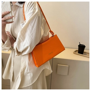 Détail du sac baguette orange vif avec lettrage fashion et bandoulière à nœud décoratif