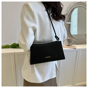 Détail du sac baguette minimaliste en cuir noir avec lettrage doré porté à l'épaule
