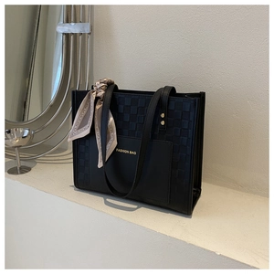 Detail of black tote bag featuring woven texture contrast and decorative silk scarf handle