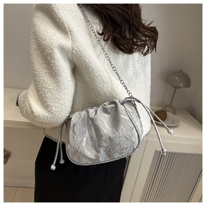 Silver metallic pleated cloud bag with chain strap shown on model's shoulder in white coat