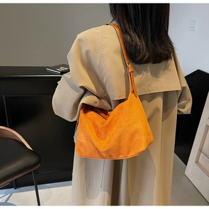 Close-up of vibrant orange suede hobo bag with adjustable strap worn on a beige coat