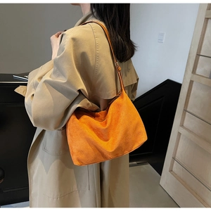 Close-up of bright orange suede hobo bag worn by model in a classic khaki trench coat