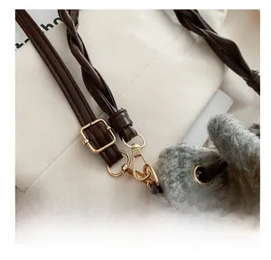 Close-up of adjustable brown braided leather strap with gold metal buckle on plush grey bag