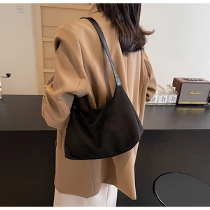 Detail of minimalist black suede hobo bag with leather strap on a beige blazer