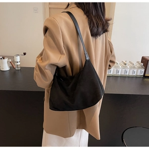 Close-up of a black suede hobo bag with leather strap worn by a woman in a brown blazer
