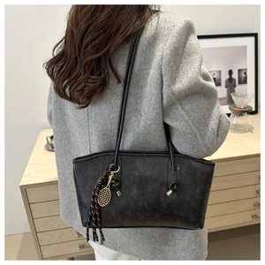 Detail view of large black tote bag with long shoulder straps and tennis racket pendant
