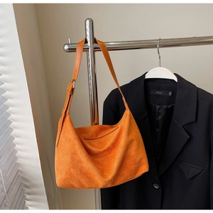 Detail of bright orange suede hobo tote bag featuring adjustable leather shoulder strap