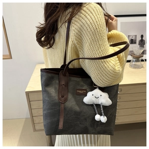 Gray canvas tote bag with brown leather straps and a plush cloud charm on a model