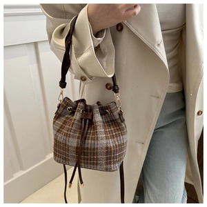 Close-up of vintage plaid tweed bucket bag with drawstring and leather trim on a model