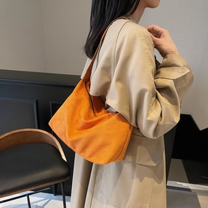 Bright orange suede hobo bag with brown strap styled on a model in a trench coat