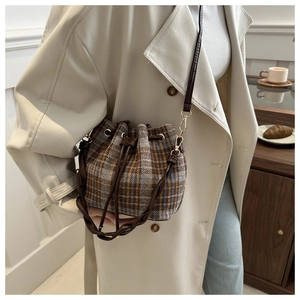 Detail view of a plaid bucket bag styled with a beige trench coat for a casual look