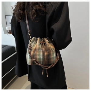 Detail of plaid bucket bag with braided handle and chain strap on black blazer