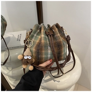 Detail of plaid bucket bag with plush fabric texture, drawstring, and monster charm