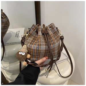 Detail of plaid bucket bag with brown leather strap and plush doll charm on mirror