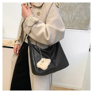 Close-up of black textured leather shoulder bag with cute plush bear charm decoration
