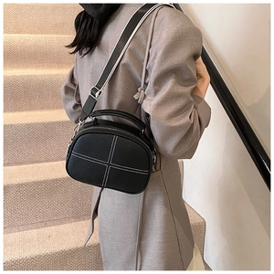 Detail of black pebbled crossbody bag featuring white cross-stitching and two-tone strap