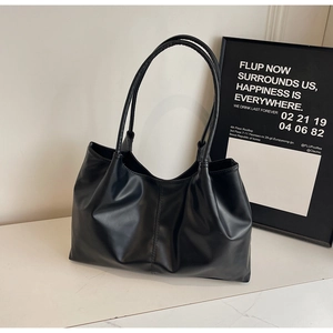 Detail of black faux leather tote bag with soft folds and fine stitching on marble surface