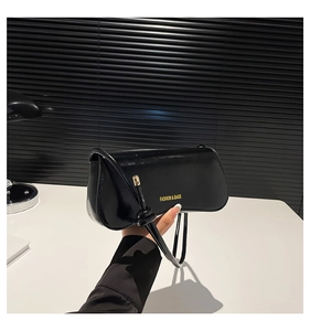Detalle de bolso de hombro en charol negro con correa anudada y letras doradas de moda