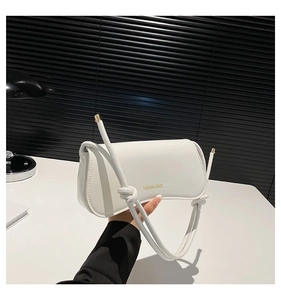 Detalle del bolso baguette blanco minimalista con correa anudada y adornos dorados finos