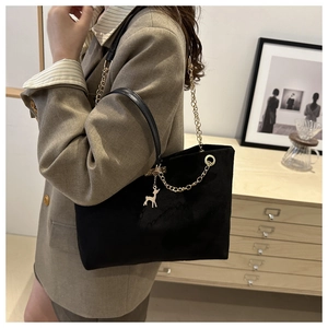 Détail du sac cabas noir avec chaîne dorée et pendentif cerf porté à l'épaule par un mannequin