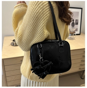 Detalle del bolso de hombro negro brillante con lazo de corazón en un ambiente acogedor