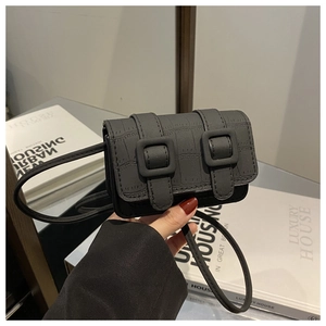 Detail van zwarte mini-crossbodytas met krokodillenreliëf en dubbele gespsluitingen