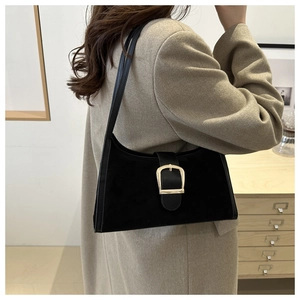 Detail of a black suede shoulder bag with a large gold D-ring buckle worn by a model