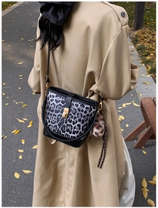 Détail du sac seau automnal à motif léopard avec boucle dorée et pompon sur un manteau