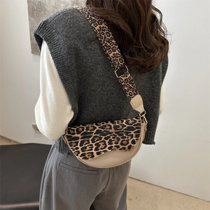 Chic leopard print saddle bag with wide shoulder strap worn by model in a minimalist setting