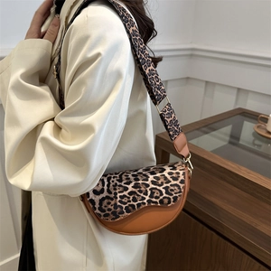 Chic leopard print saddle bag with adjustable strap worn on a stylish neutral blazer