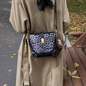 Sac seau léopard classique avec fermoir doré et breloque peluche sur un trench-coat