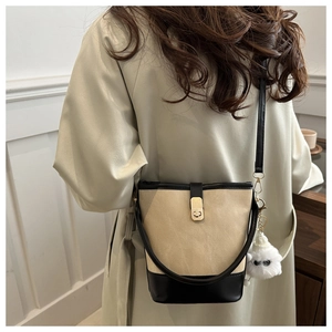 Detail of two-tone bucket bag with gold clasp and plush pendant on a model