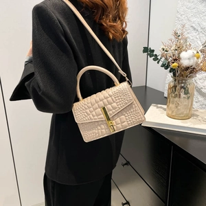 Sac à main beige élégant à motif crocodile et boucle dorée porté par un mannequin