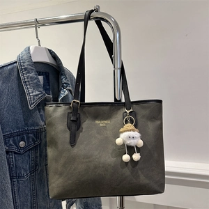 Detail of grey-green suede tote bag with golden lettering and cute plush doll pendant